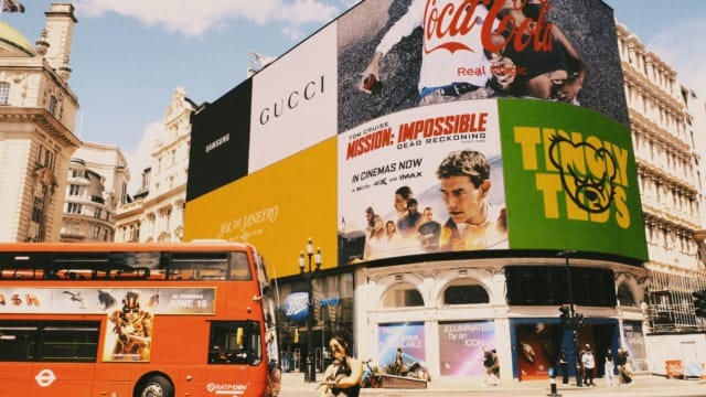 Piccadilly Circus London with Coca-Cola billboard, Mission: Impossible movie ad, red double-decker bus, people walking
