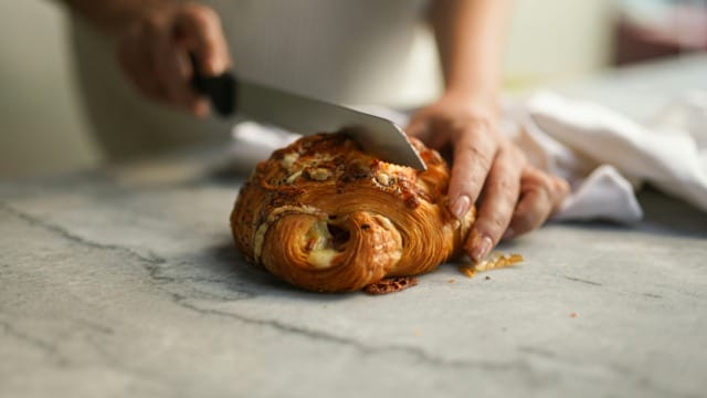 Person slicing a pastry on a marble countertop with a knife