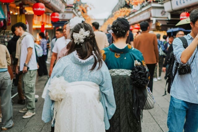 Two people in traditional clothing walking through a crowded street market with colorful decorations and lanterns.