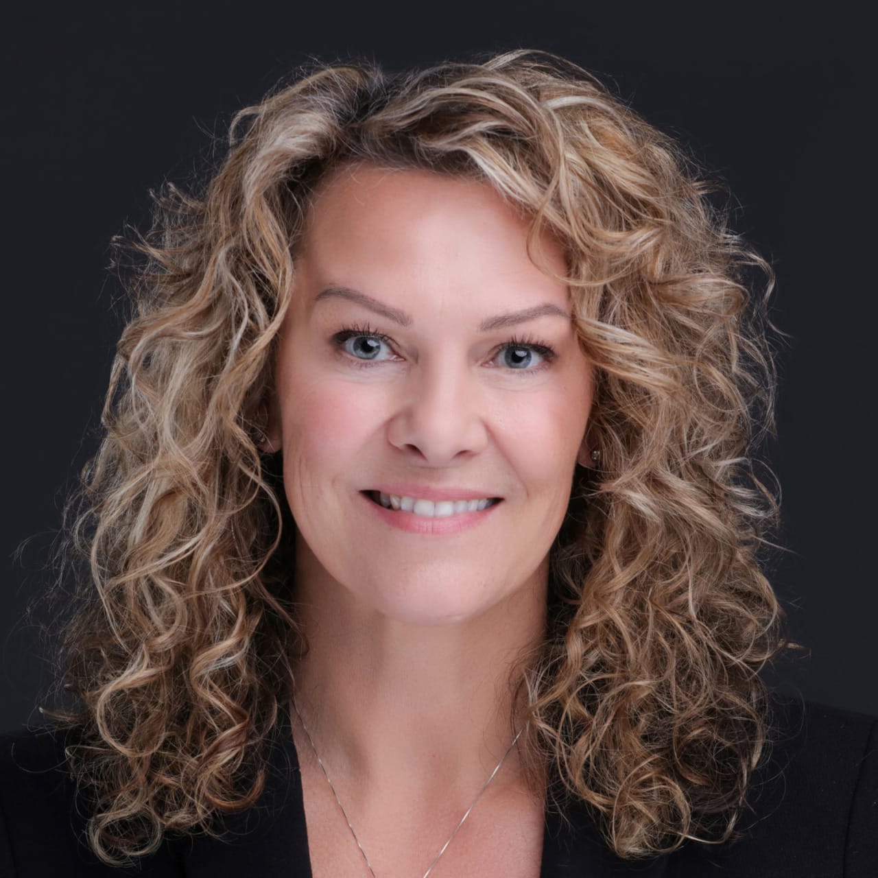 Smiling woman with curly blonde hair against a dark background.