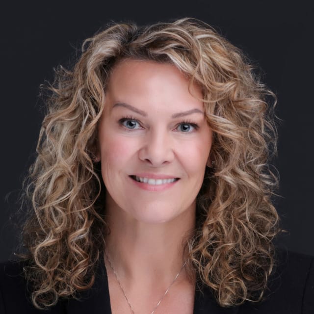 Smiling woman with curly blonde hair against a dark background.