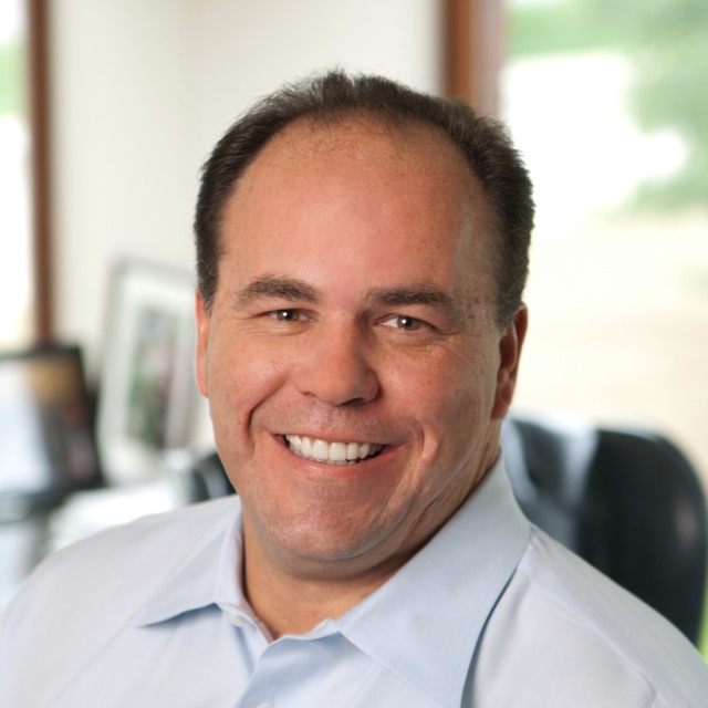 Smiling person in an office setting with blurred background.