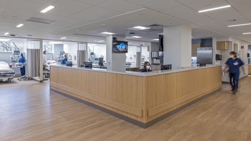Modern office space with a wooden reception desk, bright lighting, and a digital screen on the wall.