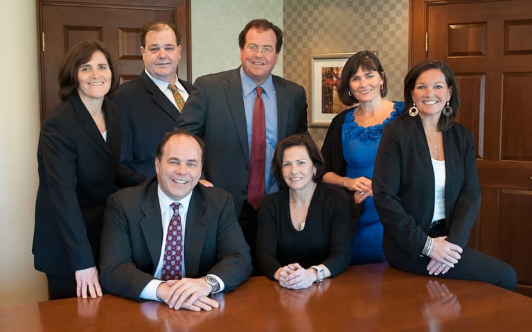 Group of eight people in business attire gathered around a conference table, smiling at the camera.
