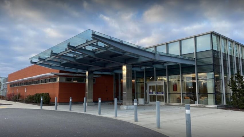 Modern building entrance with glass canopy and metal pillars under a cloudy sky.