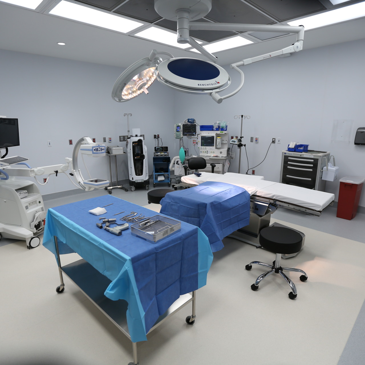 Modern surgical operating room with medical equipment, blue draped tables, and overhead lights.