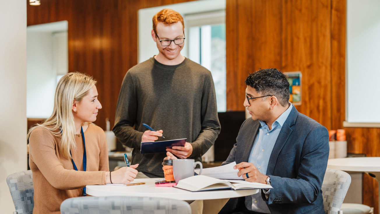 Three colleagues discussing at a round table in a modern office setting.