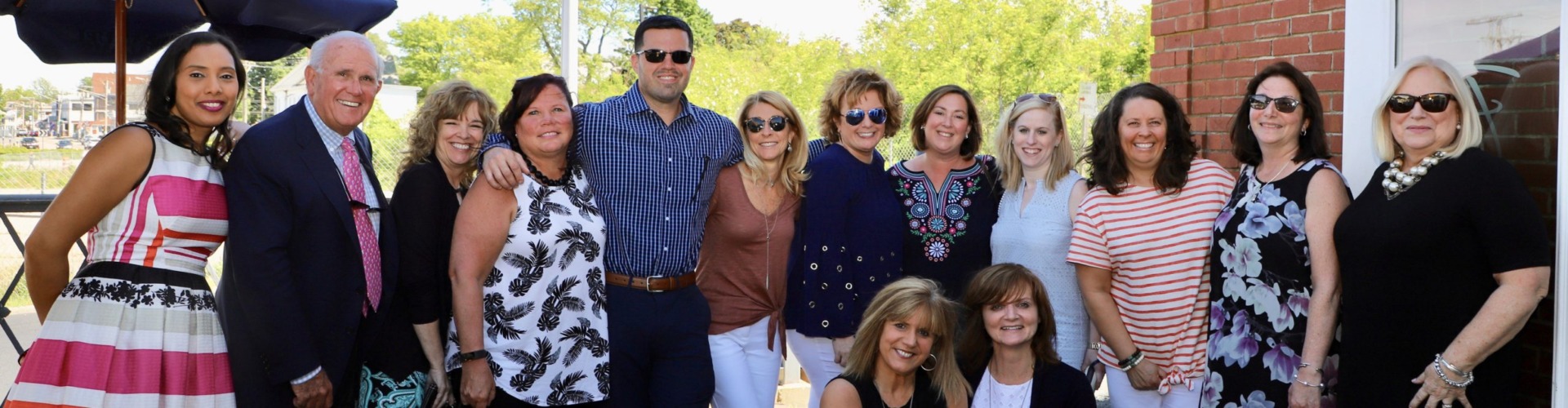 Group of people smiling outdoors with trees and a building in the background