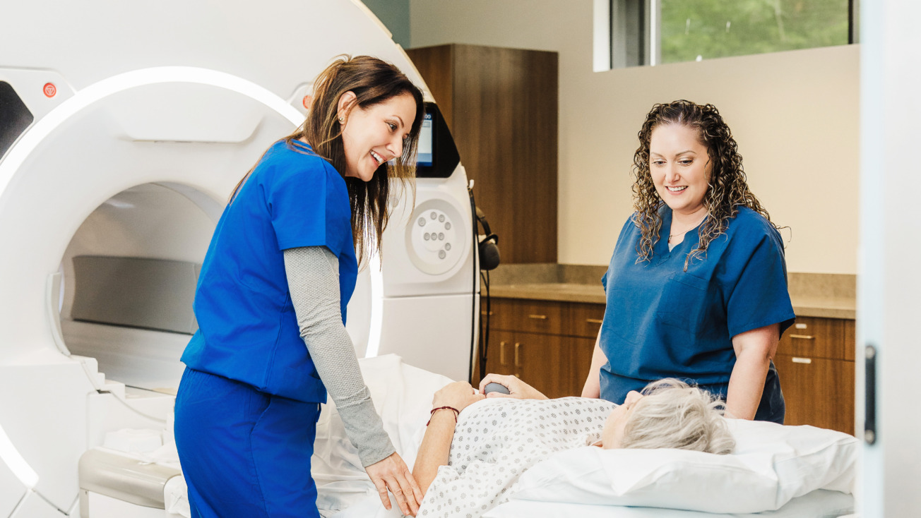 Two healthcare professionals assisting a patient lying down in a medical imaging room.