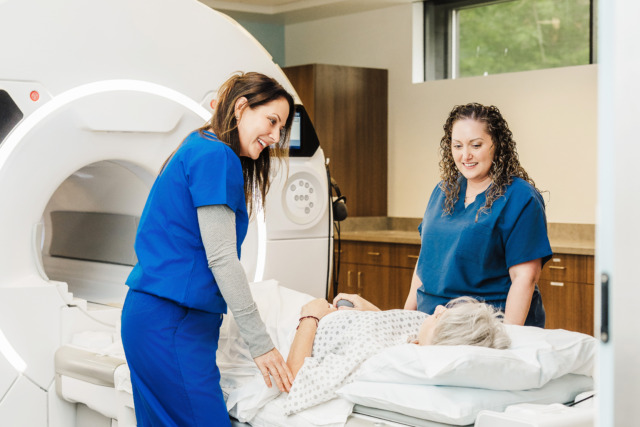 Two healthcare professionals assisting a patient lying down in a medical imaging room.