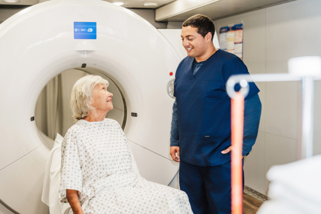 Doctor and patient in a medical scan room, with the patient sitting near an MRI machine, discussing the procedure.