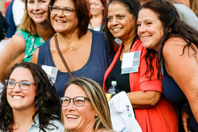 A group of smiling people posing for a photo in a stadium with empty seats in the background.