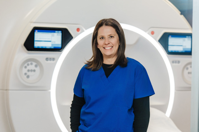 Healthcare professional in blue scrubs standing in front of medical imaging equipment in a hospital setting.