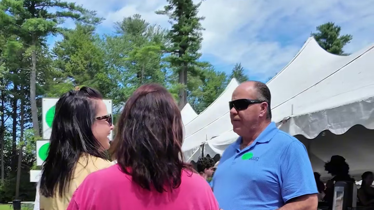 People gathered around an outdoor tent having a conversation.