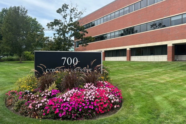 Office building with a 700 Concord Street sign, surrounded by colorful flowers and a well-maintained lawn.