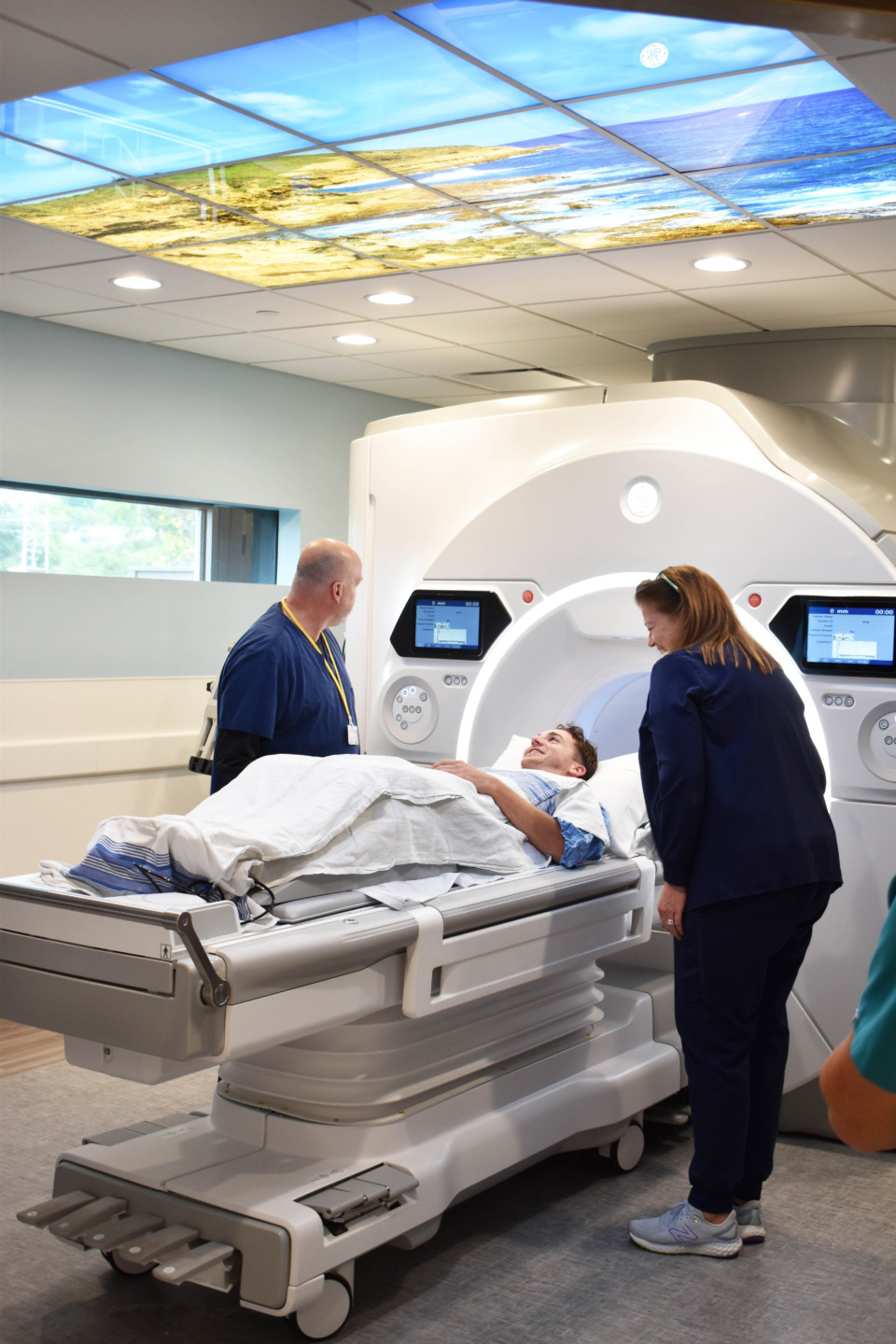 Medical staff assisting a patient lying on a bed in a modern medical imaging room with advanced equipment.
