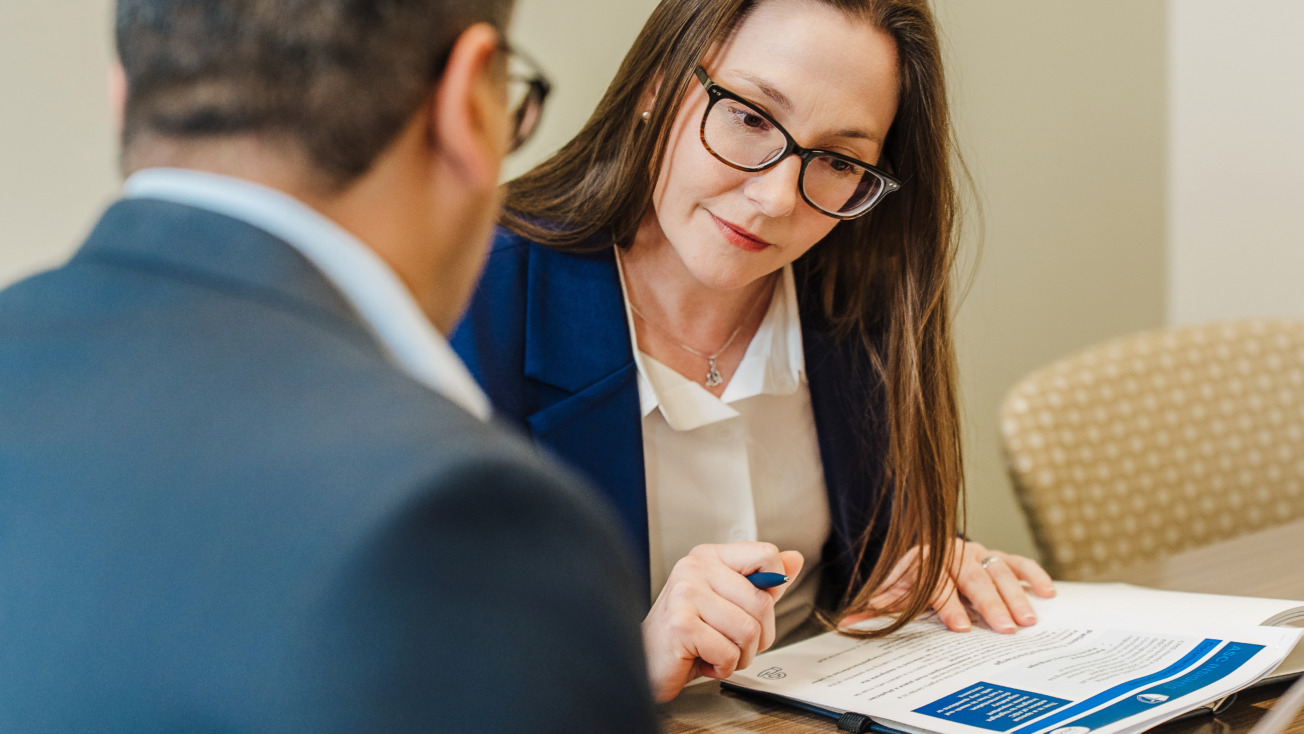 Two professionals discussing documents at a table in an office setting.