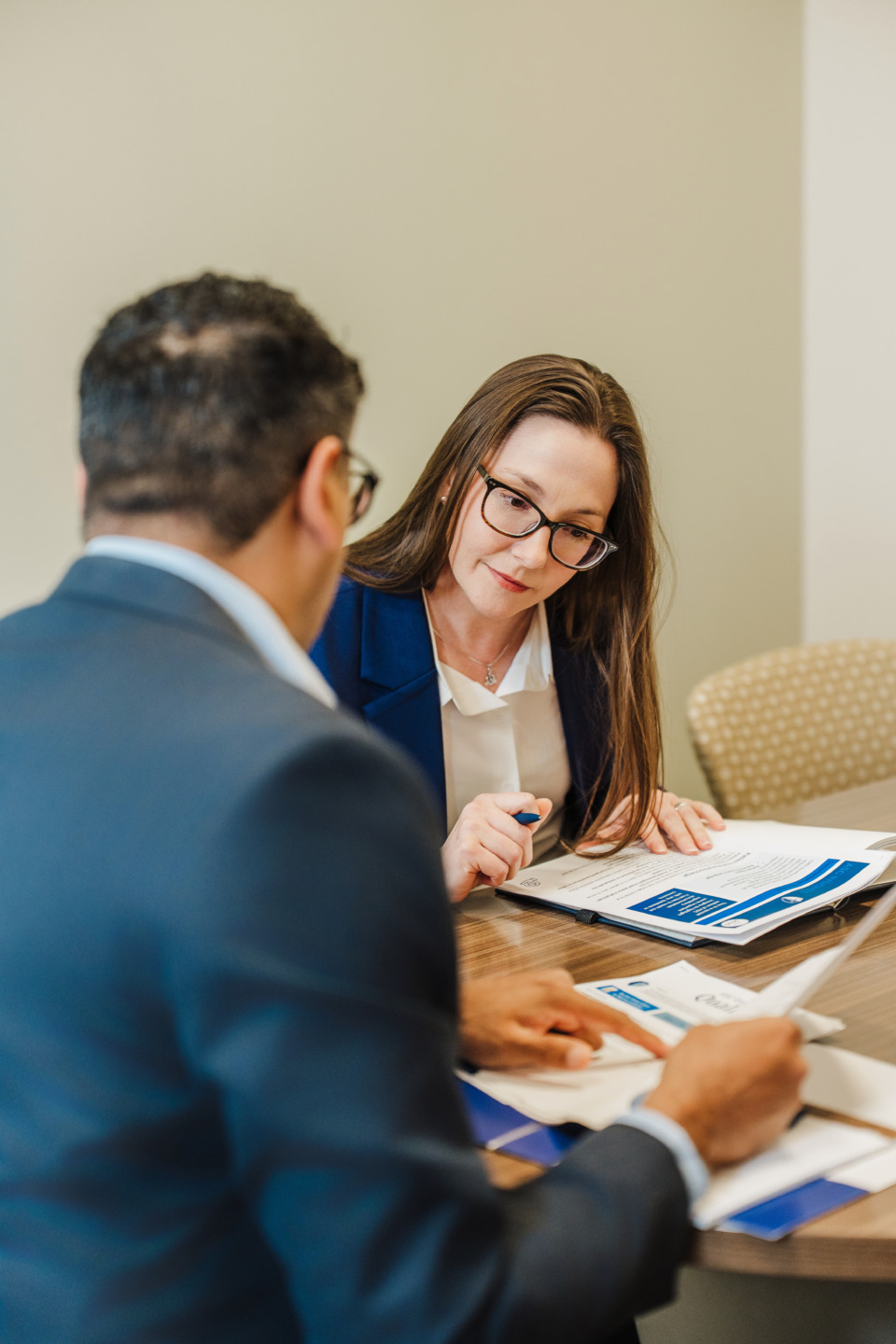 Two professionals discussing documents at a table in an office setting.