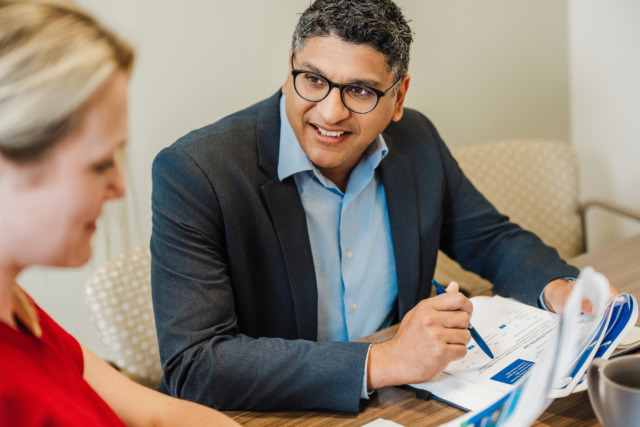 Man in a suit and woman in a red shirt have a business meeting with documents and charts on a table.