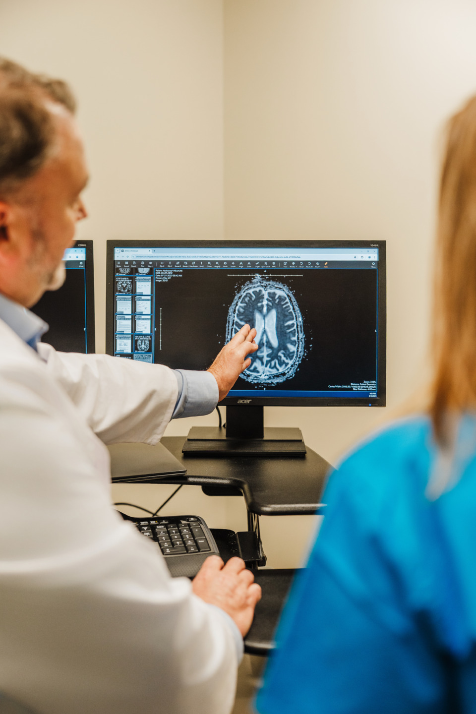 Doctor pointing at brain scan on computer monitor in medical office setting.