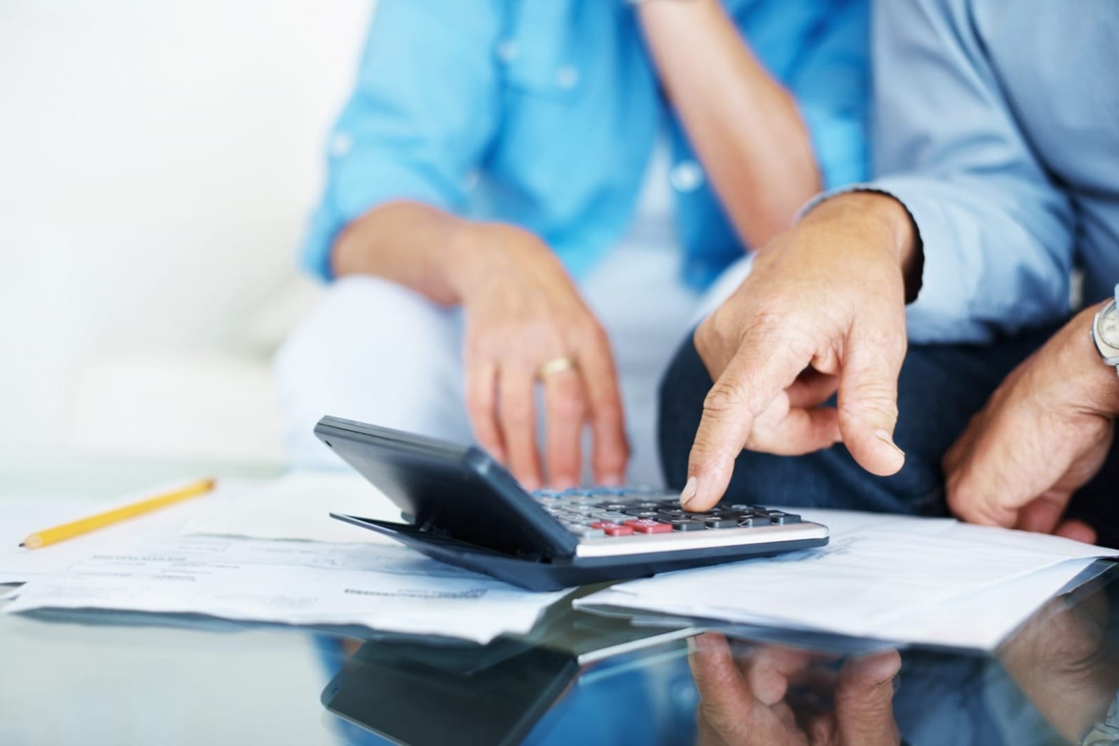 Two people sitting at a table reviewing documents and using a calculator, focusing on financial planning or budgeting.