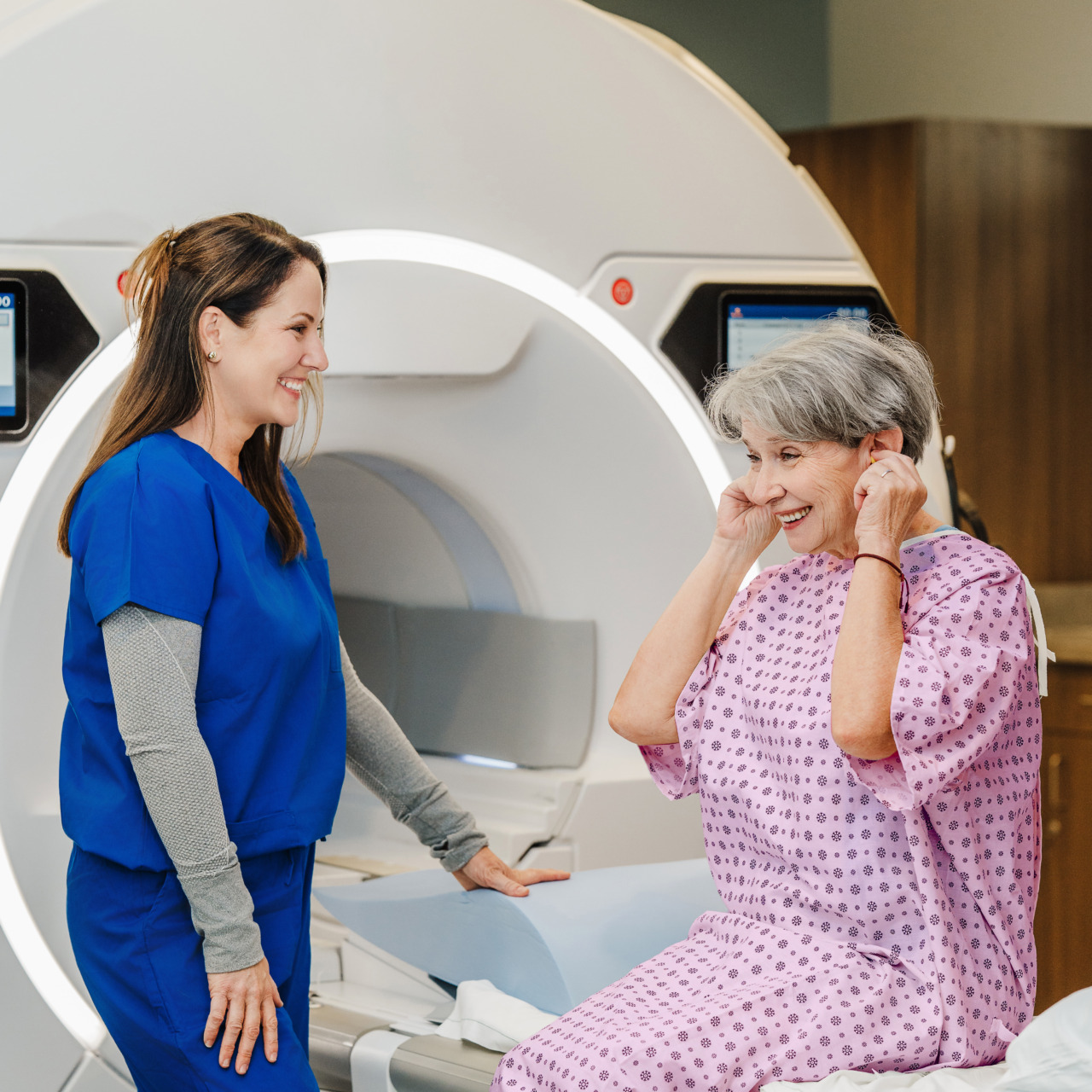 Nurse talking to a patient seated in front of an MRI machine in a medical facility.