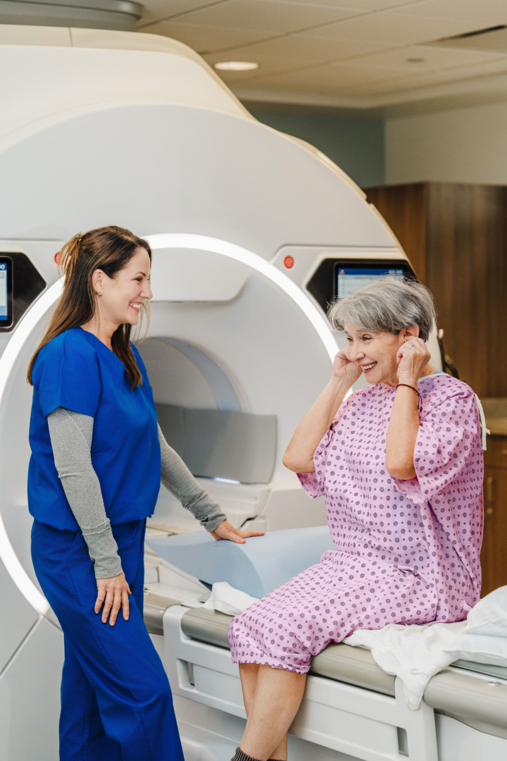 Nurse talking to a patient seated in front of an MRI machine in a medical facility.