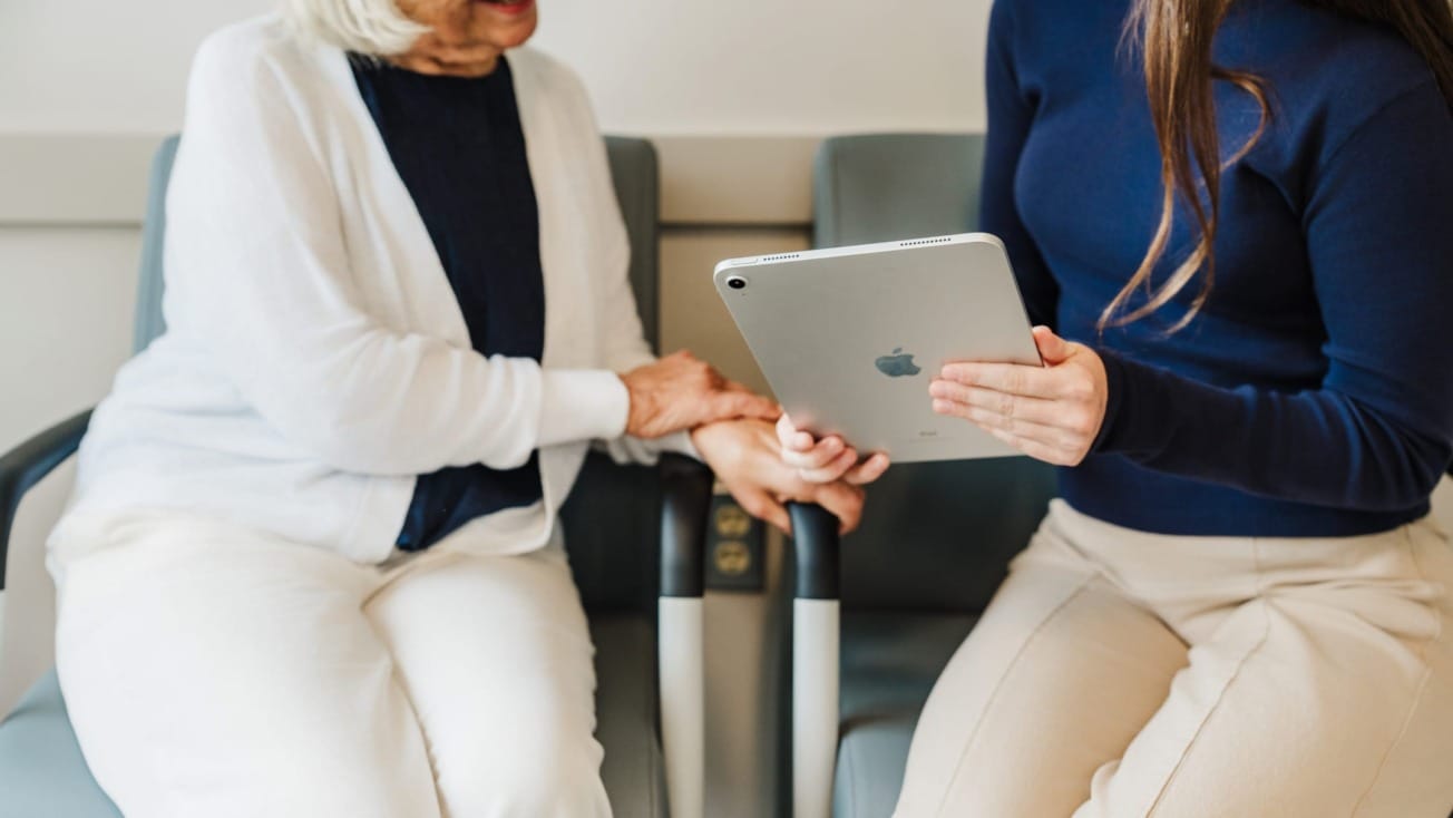 Two women sitting, one holding a tablet, having a discussion in a comfortable setting with chairs.
