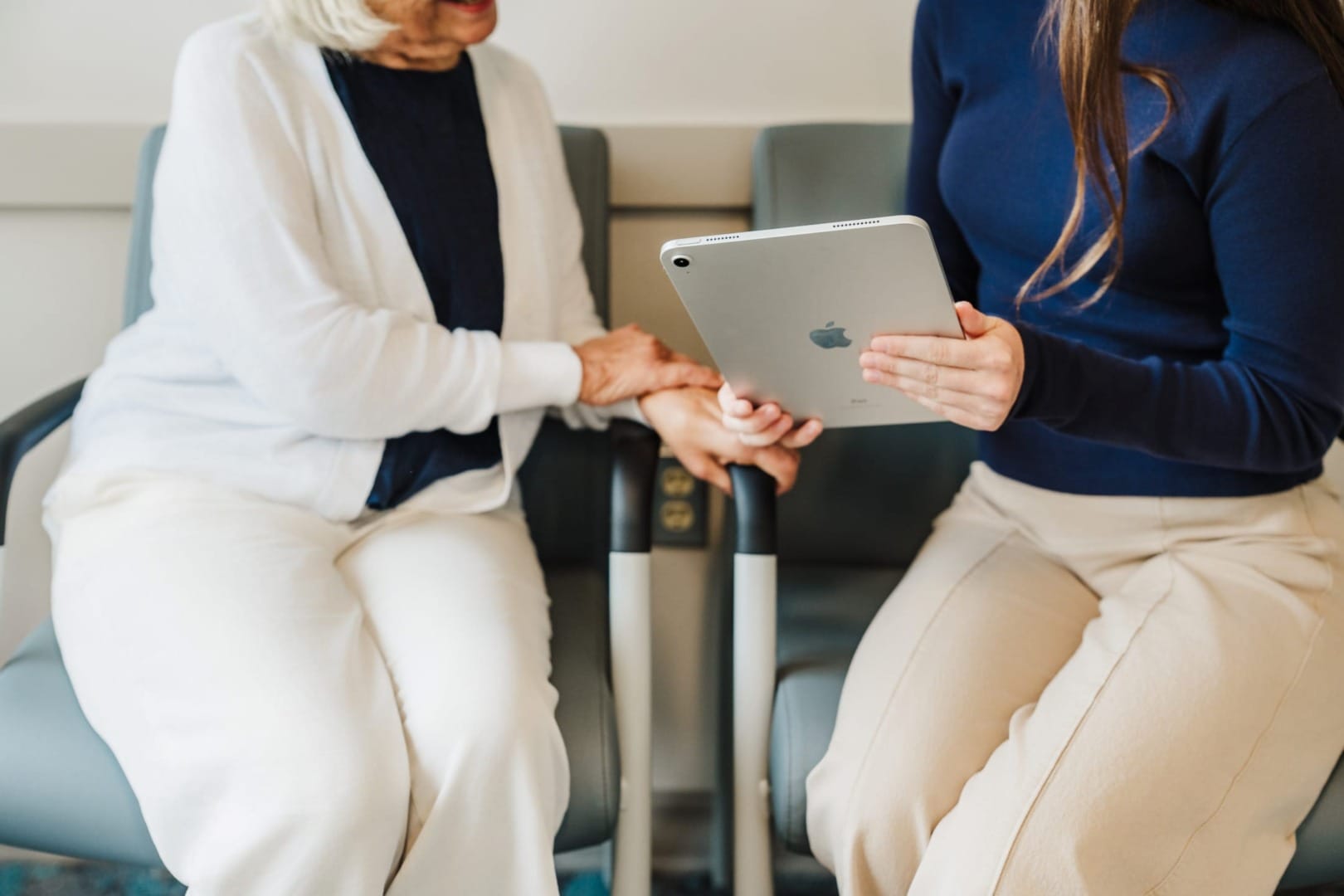 Two women sitting, one holding a tablet, having a discussion in a comfortable setting with chairs.