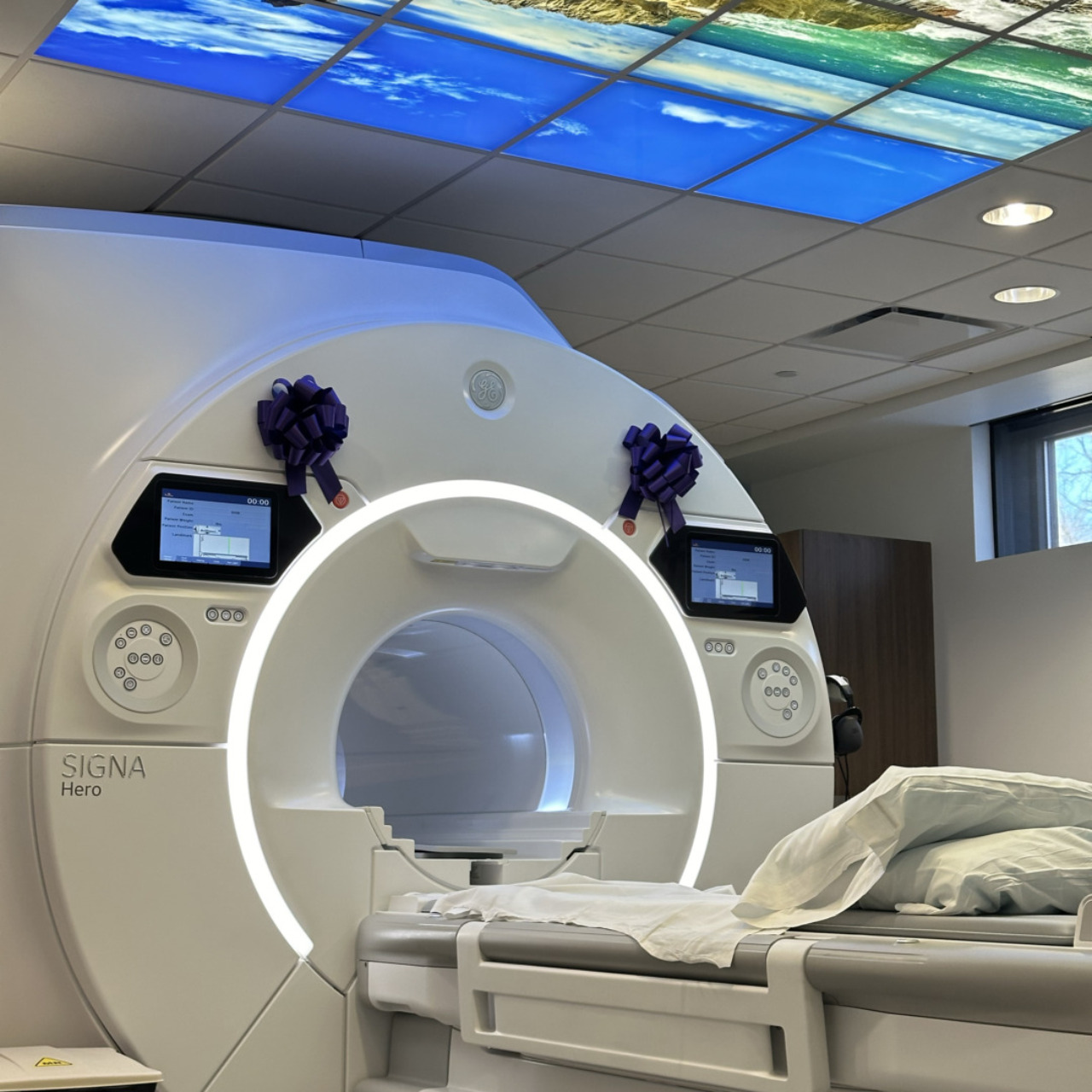 MRI machine in a hospital room with scenic ceiling panels depicting nature, complete with a patient bed.