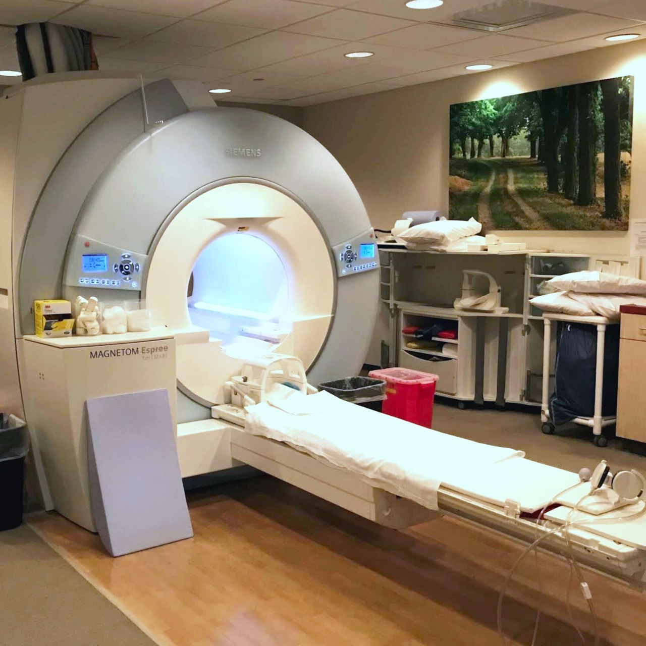 MRI machine in a hospital room with medical equipment and a nature painting on the wall in the background.