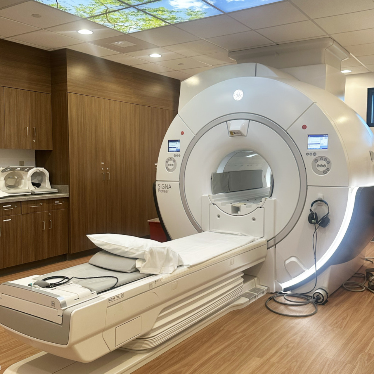 Modern MRI machine in a hospital room with wood paneling and a nature-themed ceiling design.