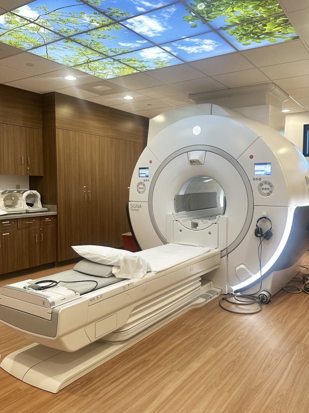 Modern MRI machine in a hospital room with wood paneling and a nature-themed ceiling design.