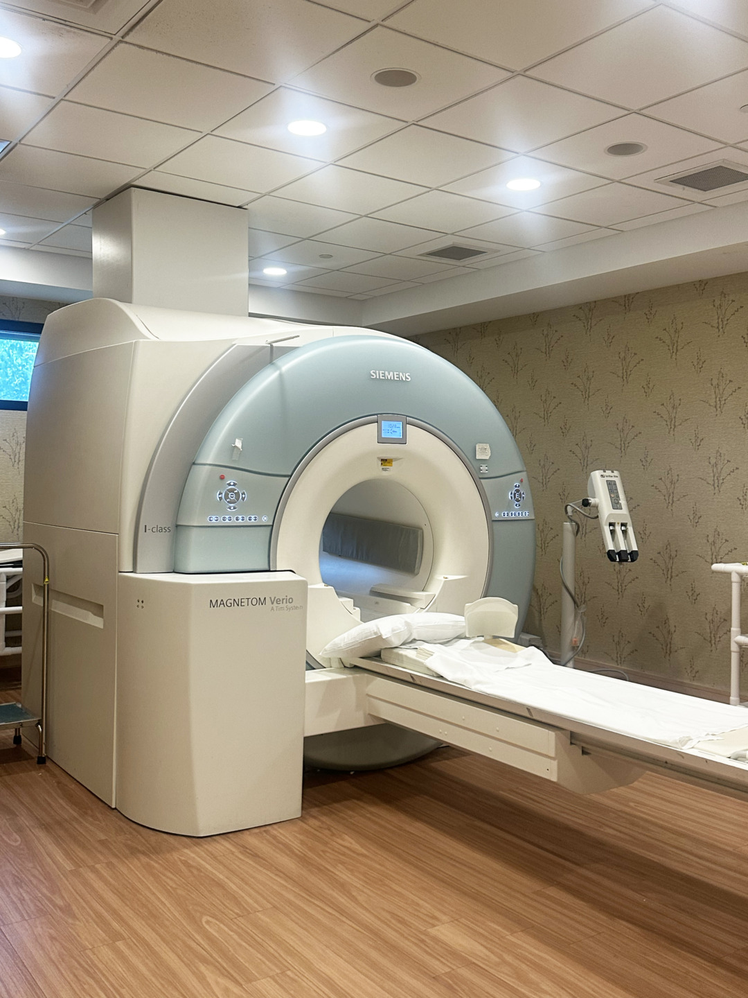 MRI machine in a medical room with wood flooring and patterned wallpaper, ready for patient use.