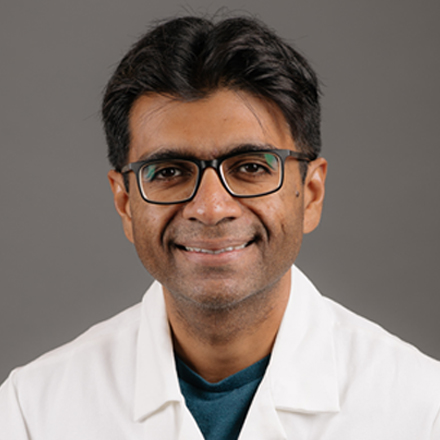 Person wearing glasses and a white coat smiling in front of a plain background.
