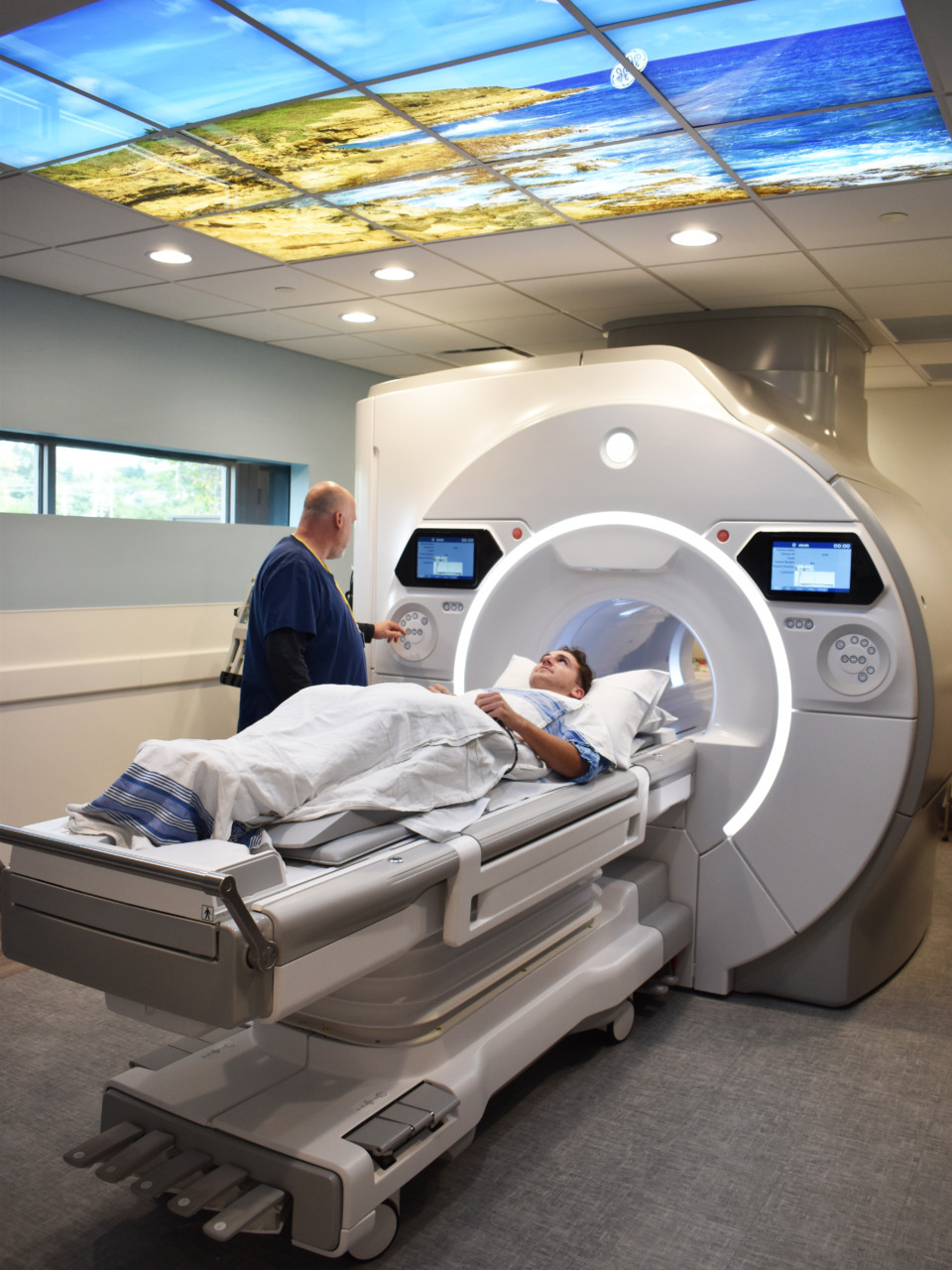 Patient undergoing MRI scan in a hospital room with a technician monitoring the procedure on a screen.