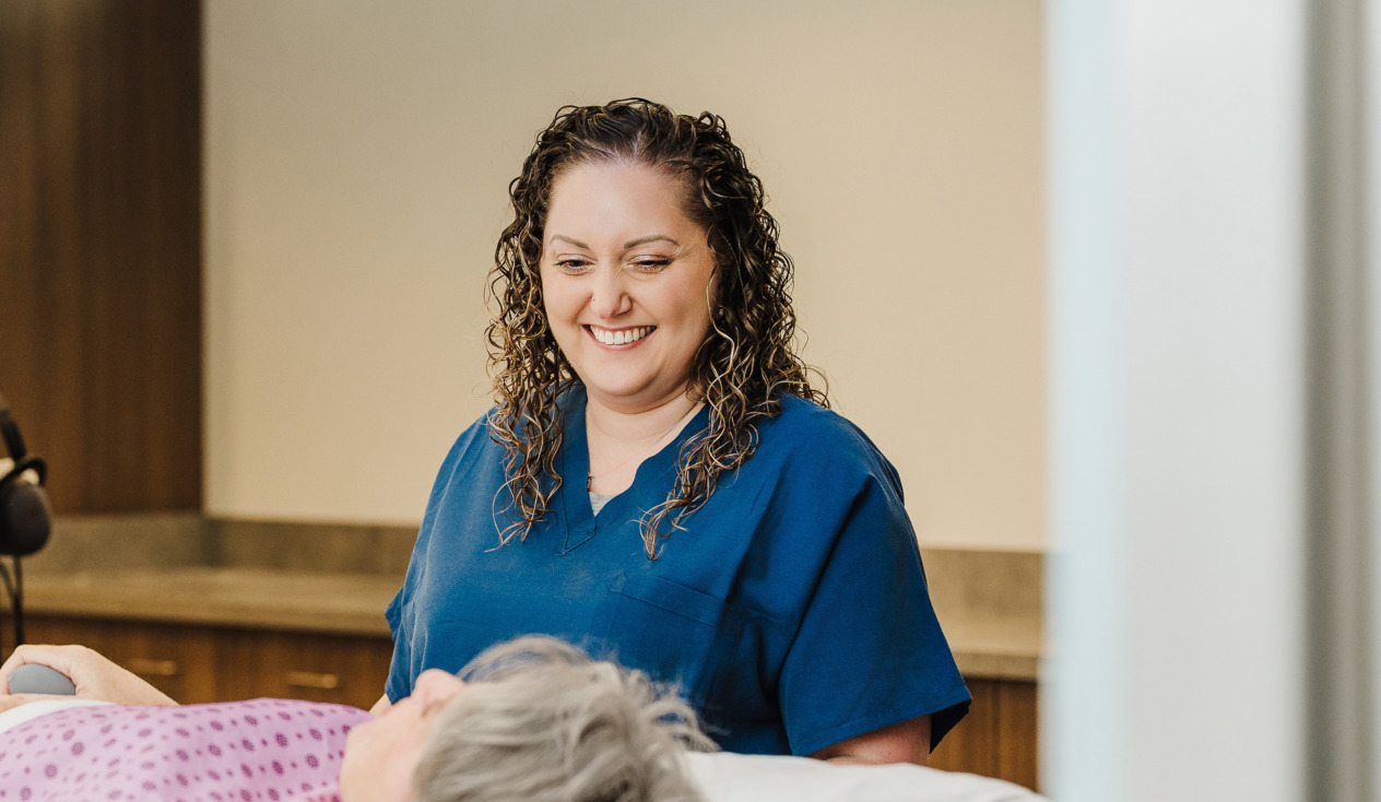 Healthcare professional smiling, standing by a patient in a hospital setting.
