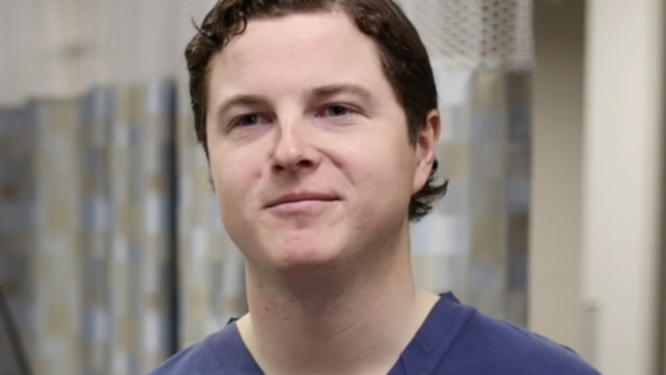 Person in blue scrubs standing in a room with a neutral expression