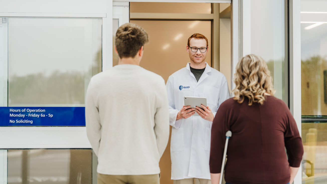 Doctor welcoming patients at a hospital entrance, one with a crutch, representing healthcare and medical assistance