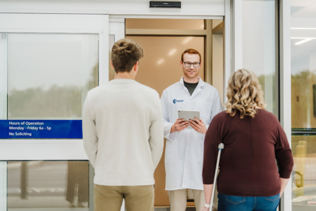 Doctor welcoming patients at a hospital entrance, one with a crutch, representing healthcare and medical assistance