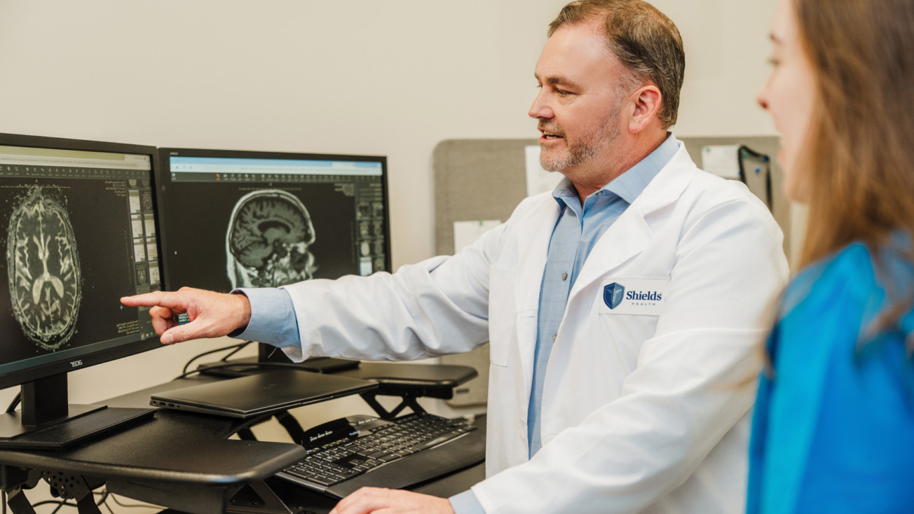 Doctor in a white coat reviewing a brain scan on a computer monitor with a colleague in a medical office.