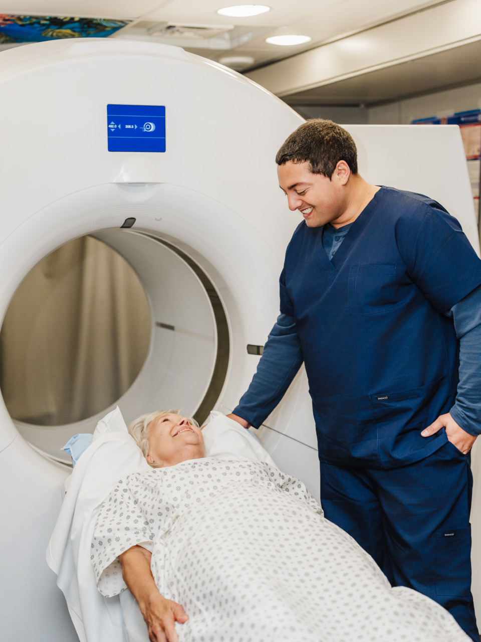 Healthcare professional assisting patient lying on a hospital bed in front of a CT scanner.