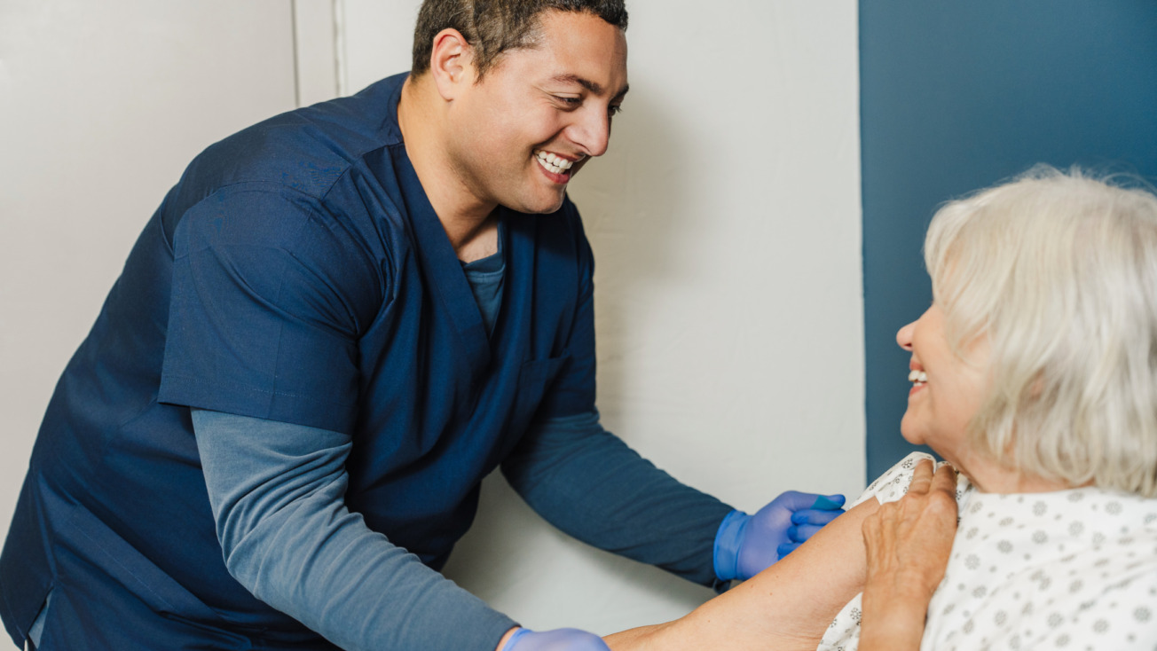 Healthcare professional administering a vaccine to a smiling older adult in a clinic setting.