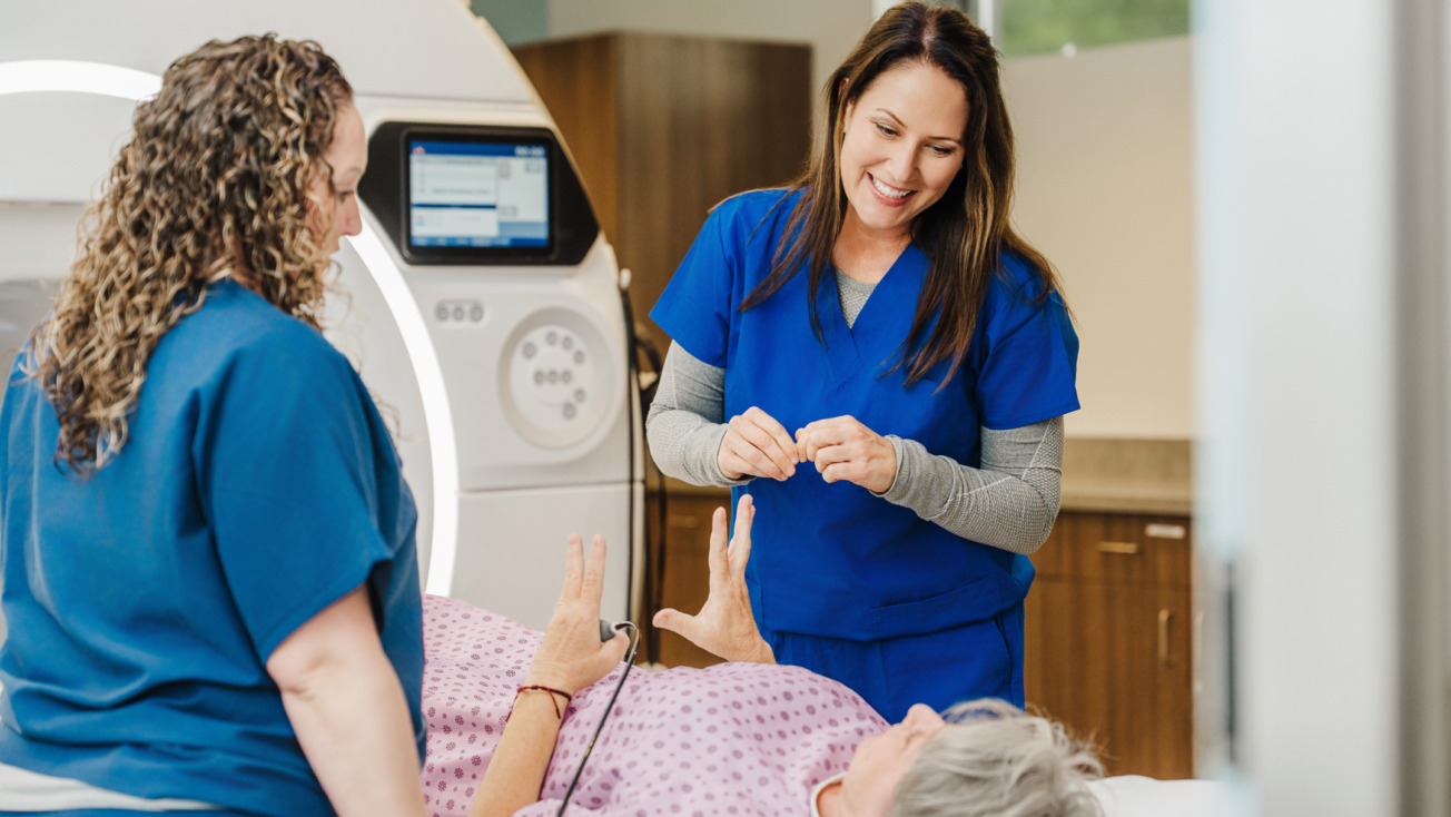 Healthcare professionals in blue scrubs assisting an elderly patient lying on a bed near medical equipment.