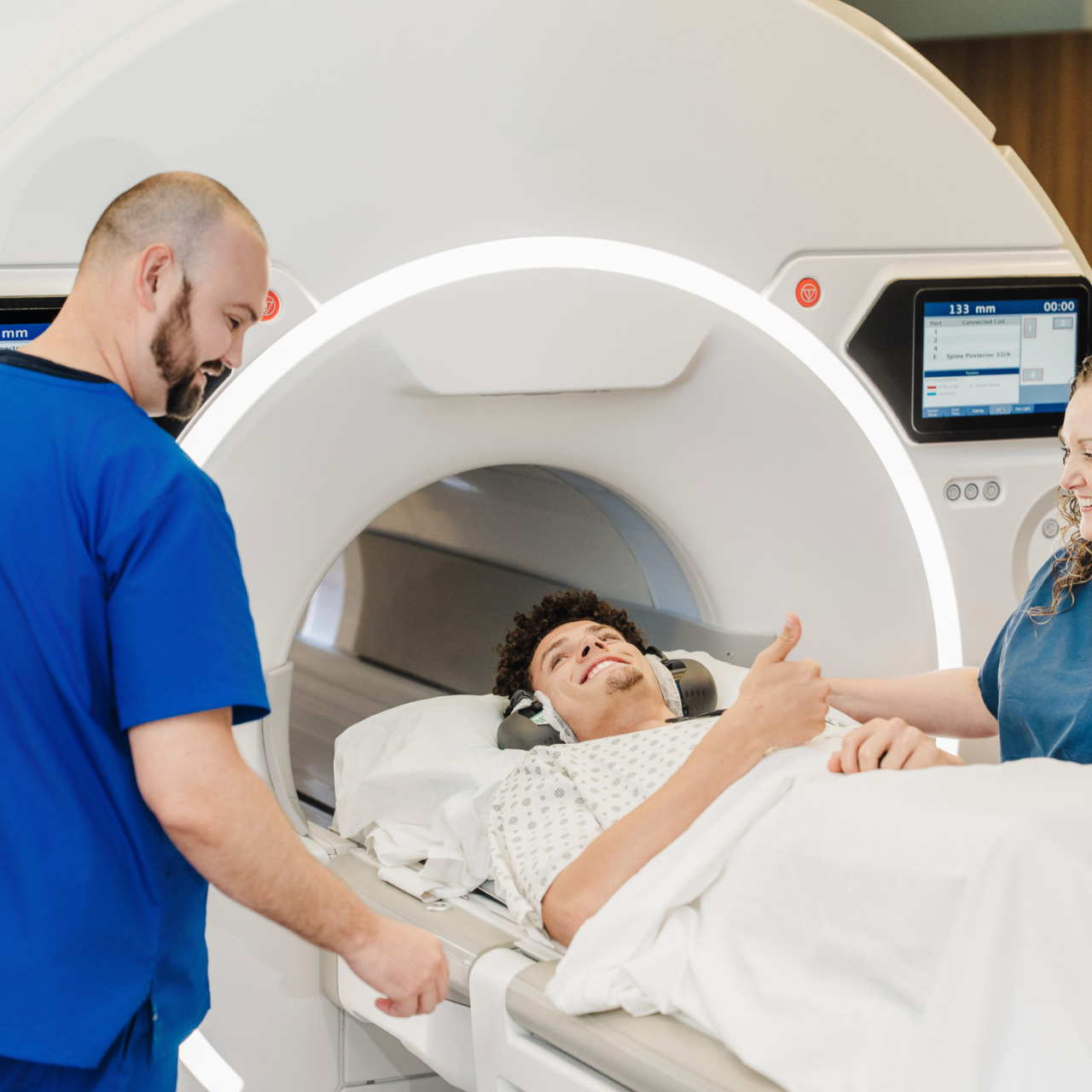 Patient giving thumbs up before MRI scan with medical staff nearby