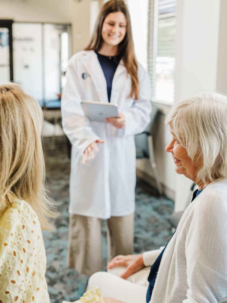Doctor in a white coat talking to two older women in a clinic waiting room.