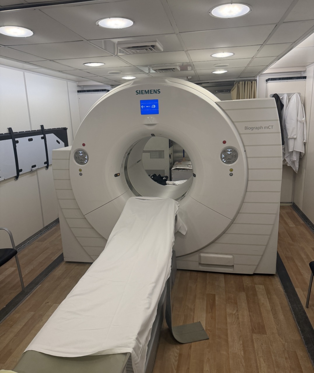 MRI machine in a clinical setting with a bed extending towards the scanner, surrounded by medical equipment and furnishings.