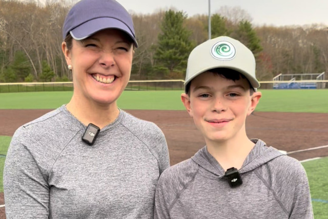 Smiling woman and boy in baseball caps standing on a baseball field.