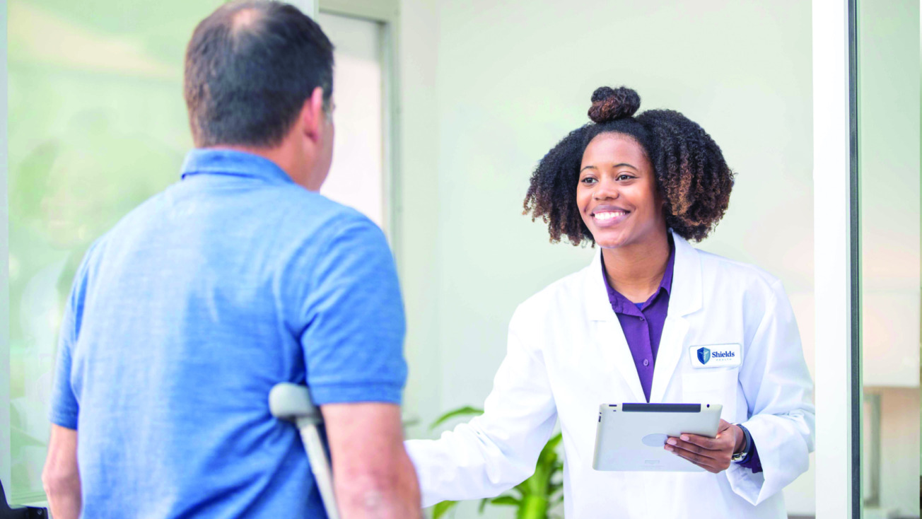 Doctor greeting a patient on crutches in a medical office setting.