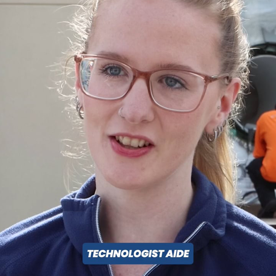 Person with glasses and a blue jacket standing outdoors, text overlay reads "TECHNOLOGIST AIDE".